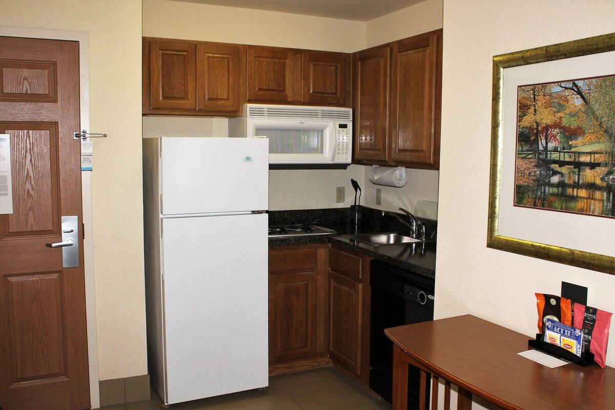 A compact kitchen with wooden cabinets, a white refrigerator, a microwave, a sink, and a stove.