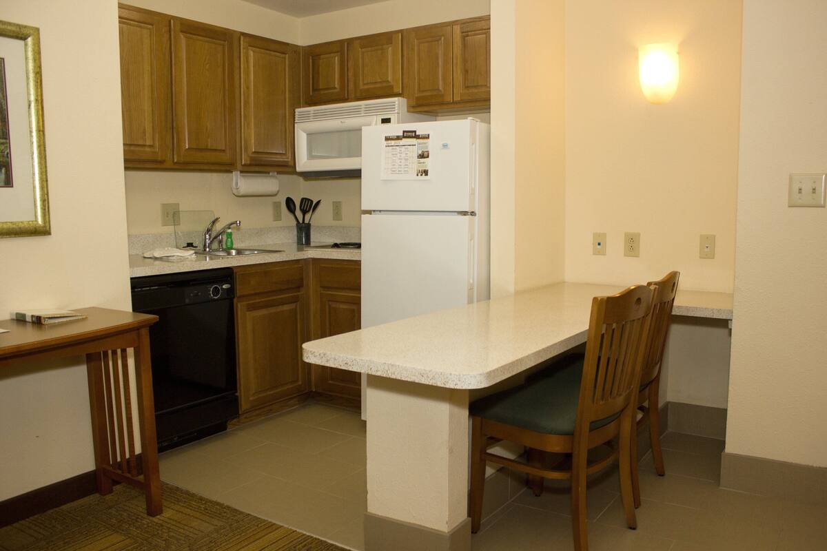 A compact kitchen with wooden cabinets, a white refrigerator, a microwave, and a dining area with a wooden table and chairs.
