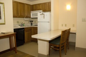 A compact kitchen with wooden cabinets, a white refrigerator, a microwave, and a dining area with a wooden table and chairs. - Staybridge Suites Houston Willowbrook by IHG (Houston)