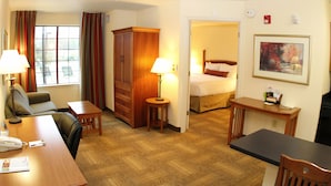 A hotel room with a wooden desk, a chair, a bed, a small table with a lamp, and a painting on the wall. - Staybridge Suites Houston Willowbrook by IHG (Houston)