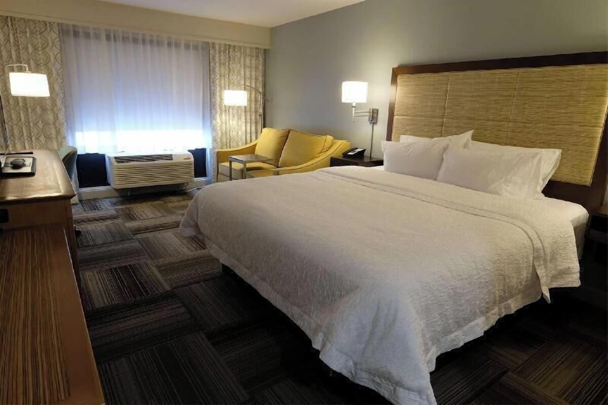 A hotel room with a large bed, a desk, a chair, and a window with curtains.
