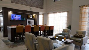 Un moderno vestíbulo de hotel con zona de comedor, asientos cómodos y una pantalla de televisión.