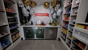 Una zona de cocina con estantes llenos de aperitivos y dulces, un refrigerador y un microondas.
