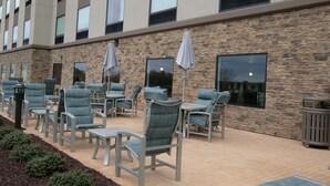 Un patio al aire libre con mobiliario y sombrillas, un muro de piedra y un edificio con amplias ventanas.