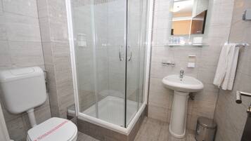 Een moderne badkamer met een douchecabine van glas, een wastafel op een voetstuk en een toilet.