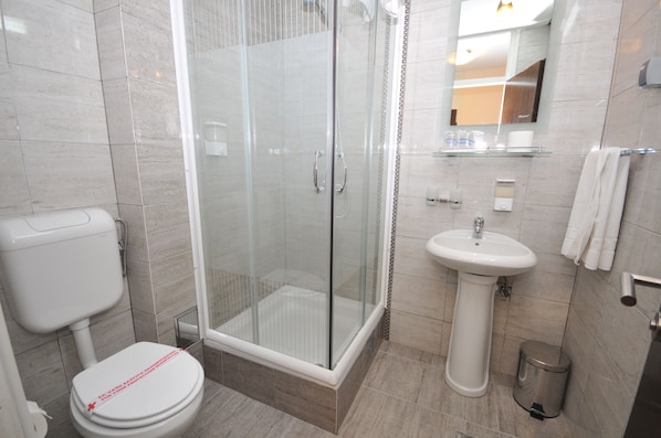 A modern bathroom with a glass-enclosed shower, a pedestal sink, and a toilet.