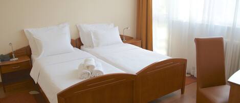 A hotel room with two single beds, a wooden chair, a desk, a nightstand, and a framed picture on the wall.
