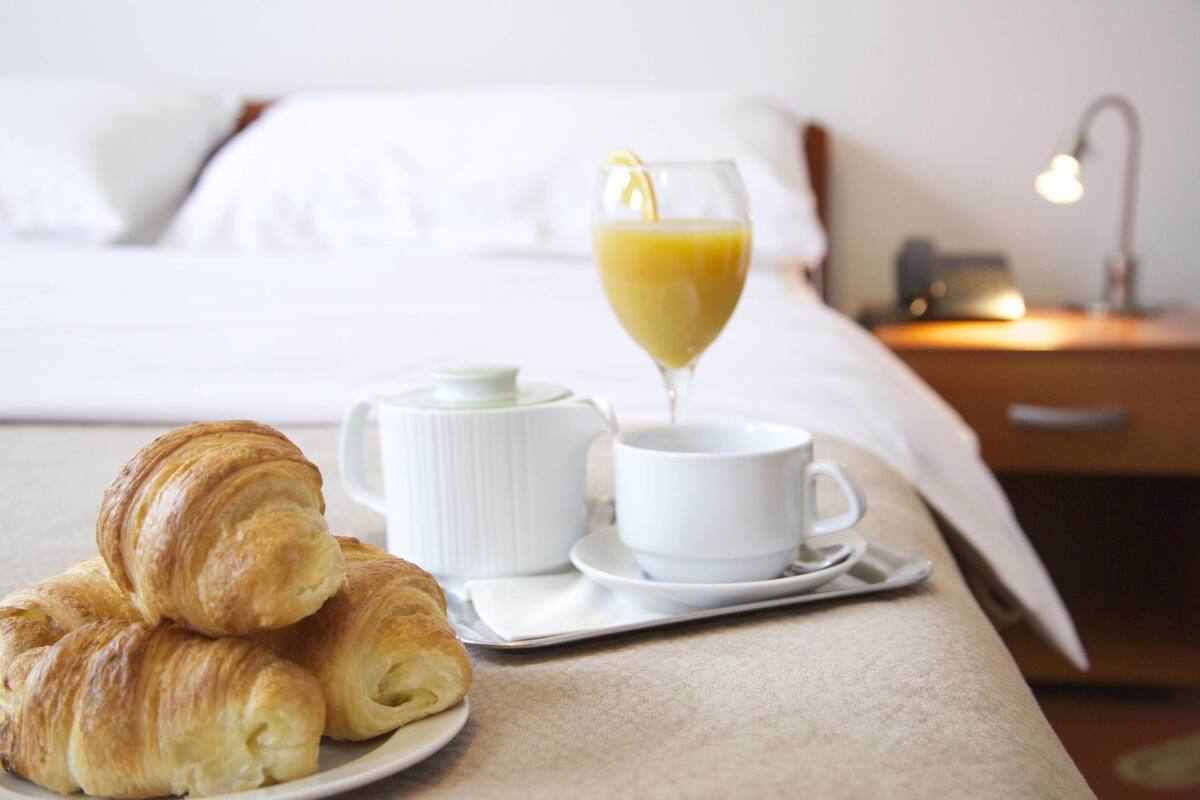 A breakfast tray with croissants, a cup of coffee, and a glass of orange juice on a bed in a hotel room.