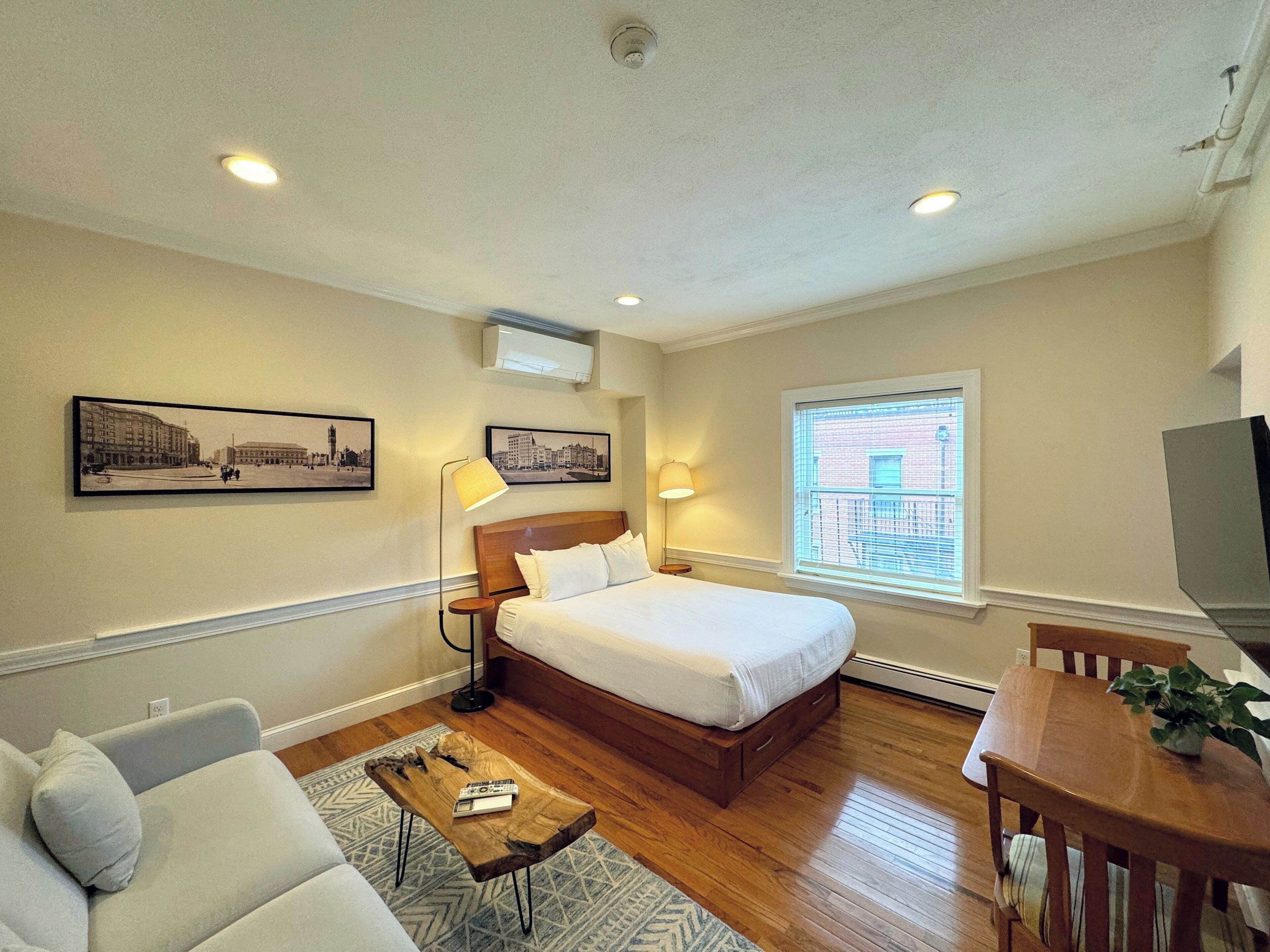 A hotel room with a bed, a desk, a chair, a sofa, a lamp, and two wall-mounted pictures.