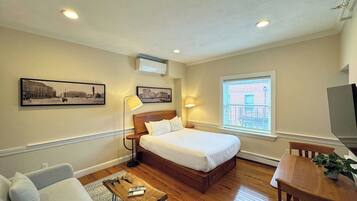 A hotel room with a bed, a desk, a chair, a sofa, a lamp, and two wall-mounted pictures.