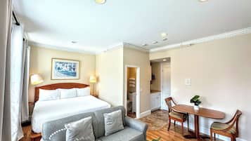 A hotel room with a bed, a grey sofa, a dining table with chairs, and a small plant.