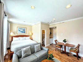A hotel room with a bed, a grey sofa, a dining table with chairs, and a small plant.