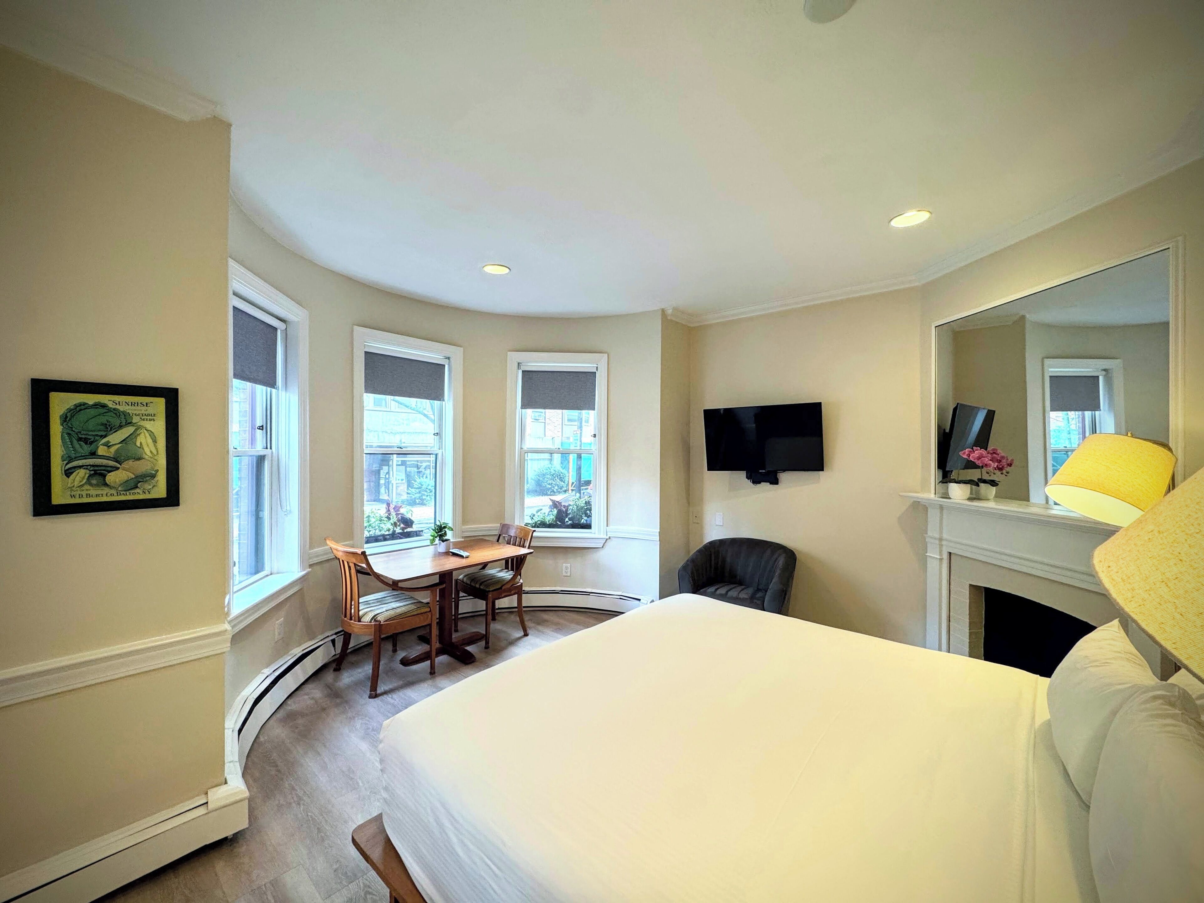 A hotel room with a bed, a desk, a chair, a television, and a fireplace.