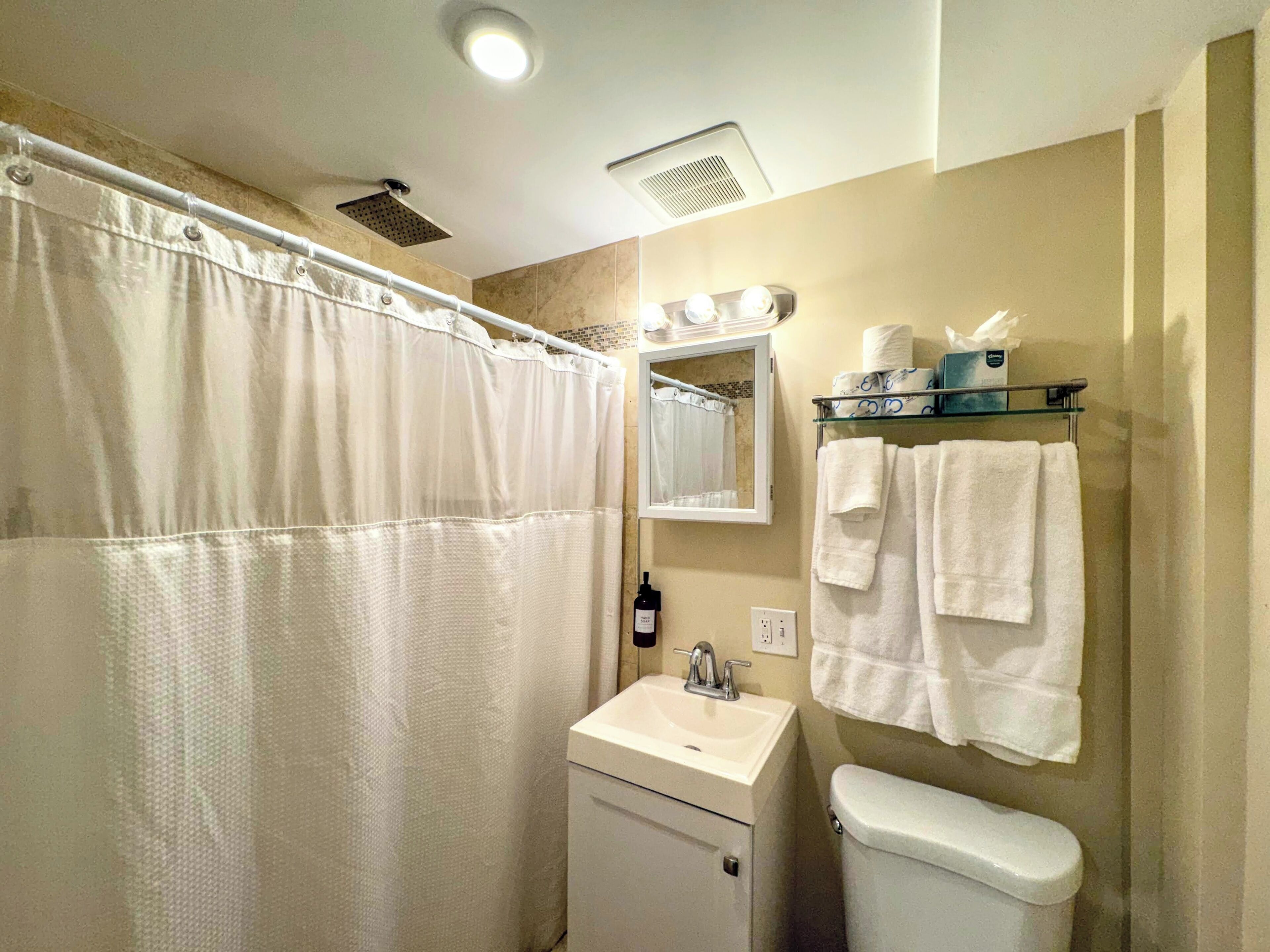 A bathroom with a shower, sink, toilet, and a mirror with lights.