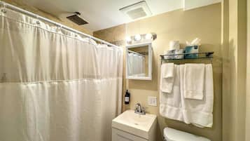 A bathroom with a shower, sink, toilet, and a mirror with lights.