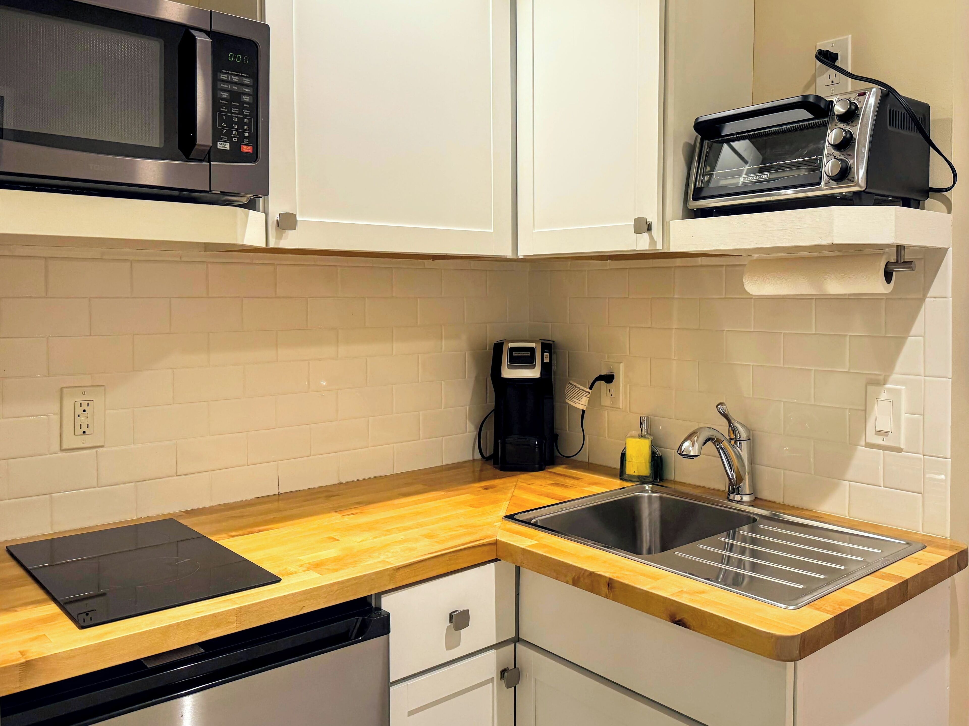 Una cocina compacta equipada con microondas, tostadora, cafetera y un lavabo con grifo.