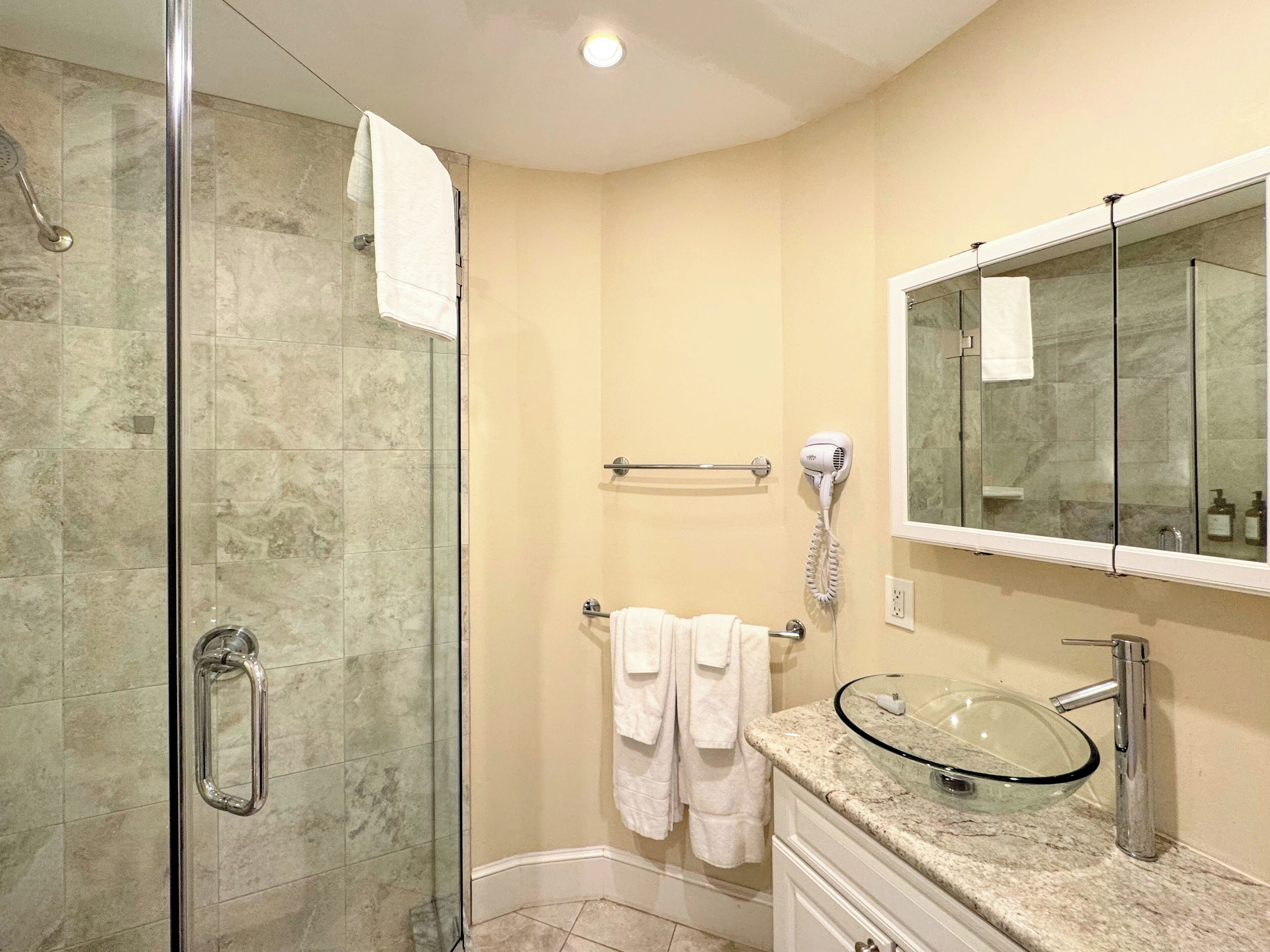 Une salle de bain avec une douche à parois de verre, un lavabo en verre et un miroir au-dessus du lavabo.