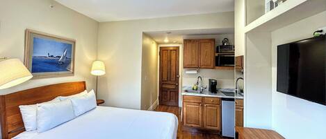 Een hotelkamer met een bed, bureau, televisie, kitchenette en een schilderij aan de muur.