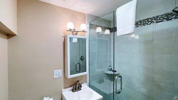 Une salle de bain moderne avec une douche à parois de verre, un lavabo blanc et un miroir au-dessus.