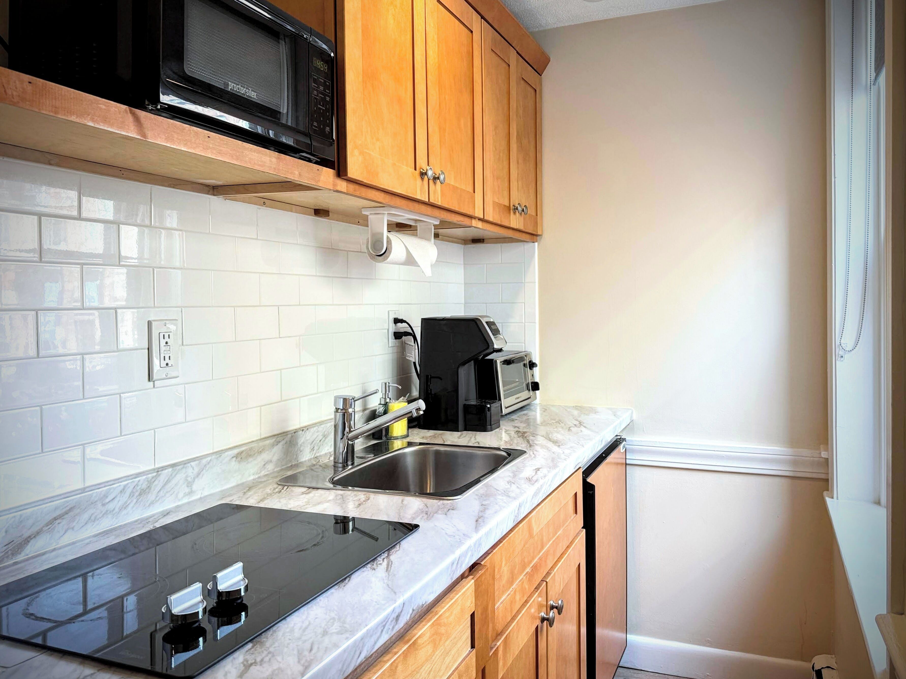 A kitchen with white subway tiles, a black microwave, a toaster, and a sink.