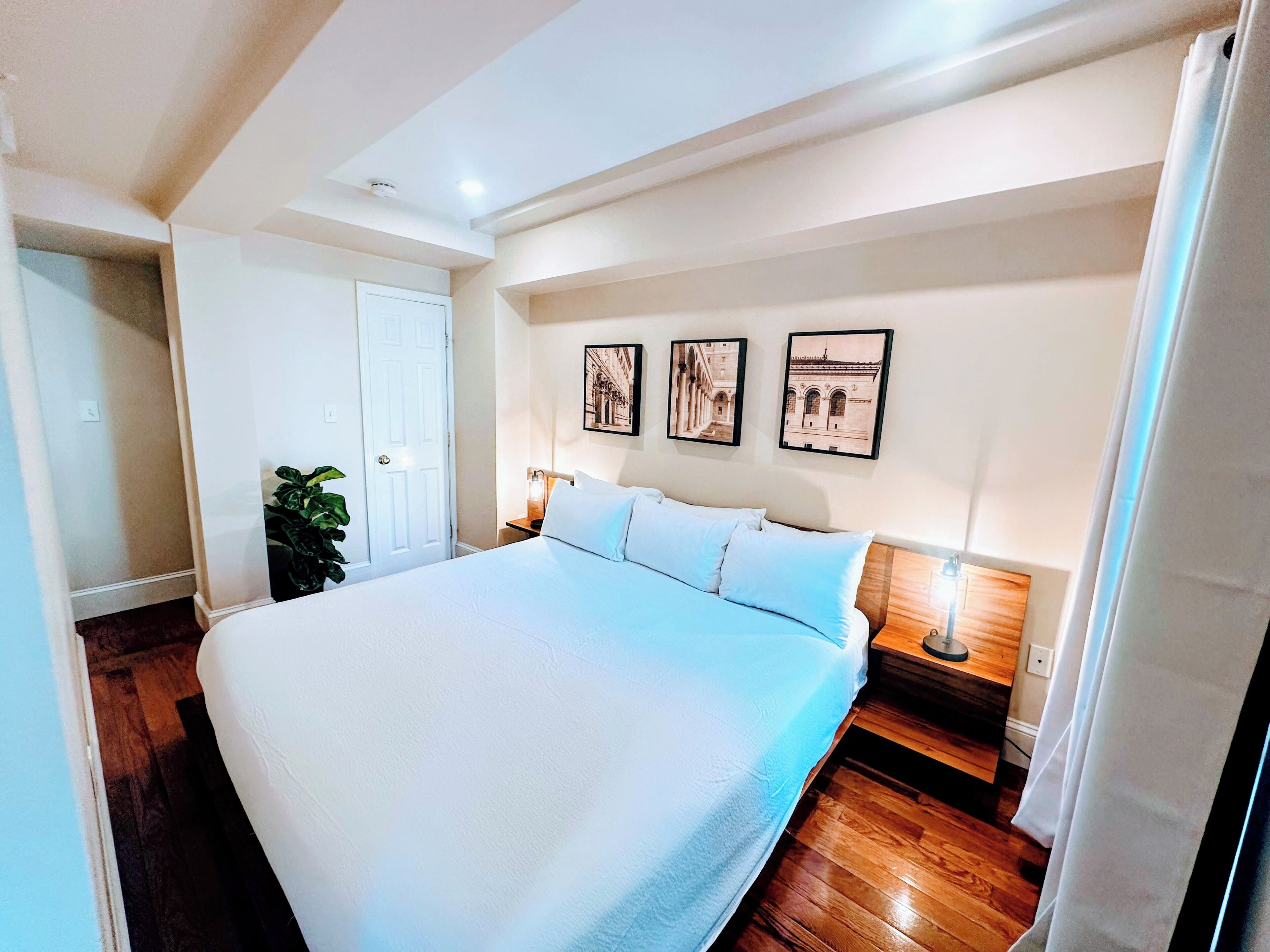 Una habitació àmplia amb un llit gran, tarima de fusta, una porta blanca i obra penjada a la paret.