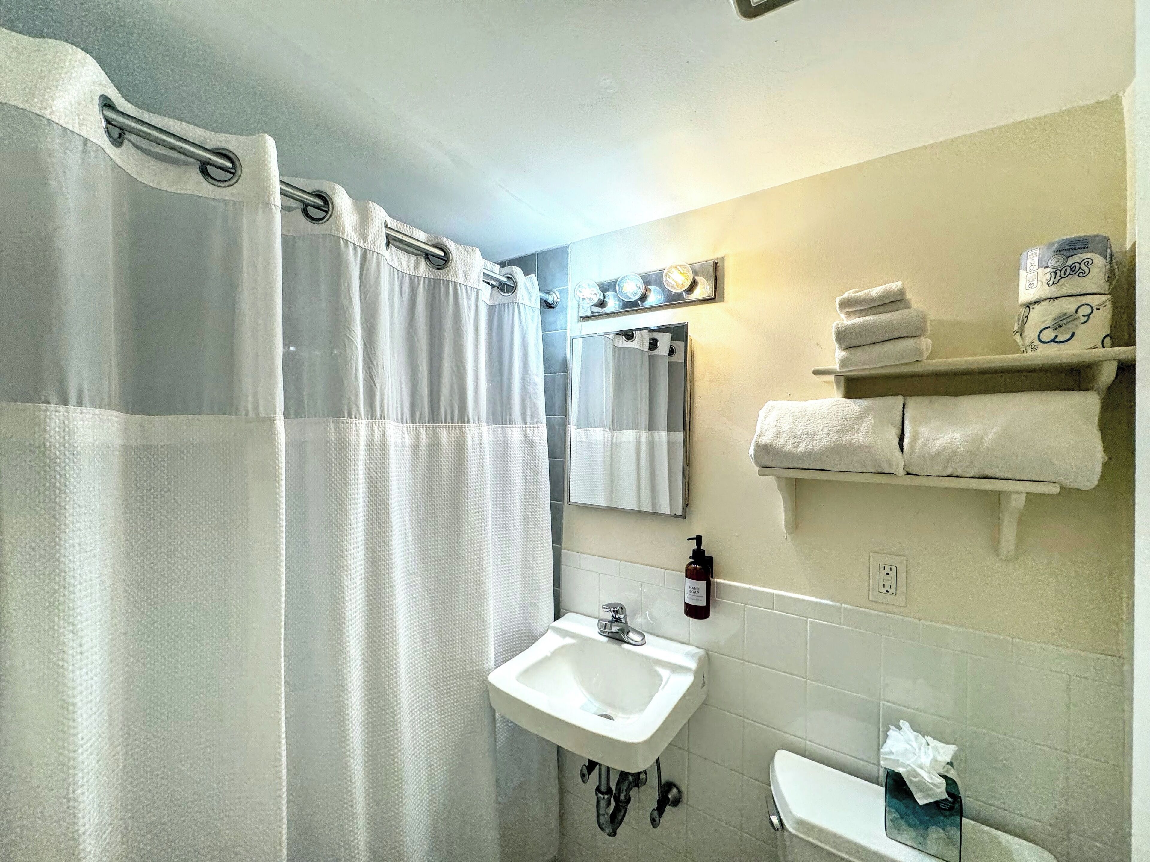 A bathroom with a shower curtain, a sink, a mirror, and a towel rack with towels.
