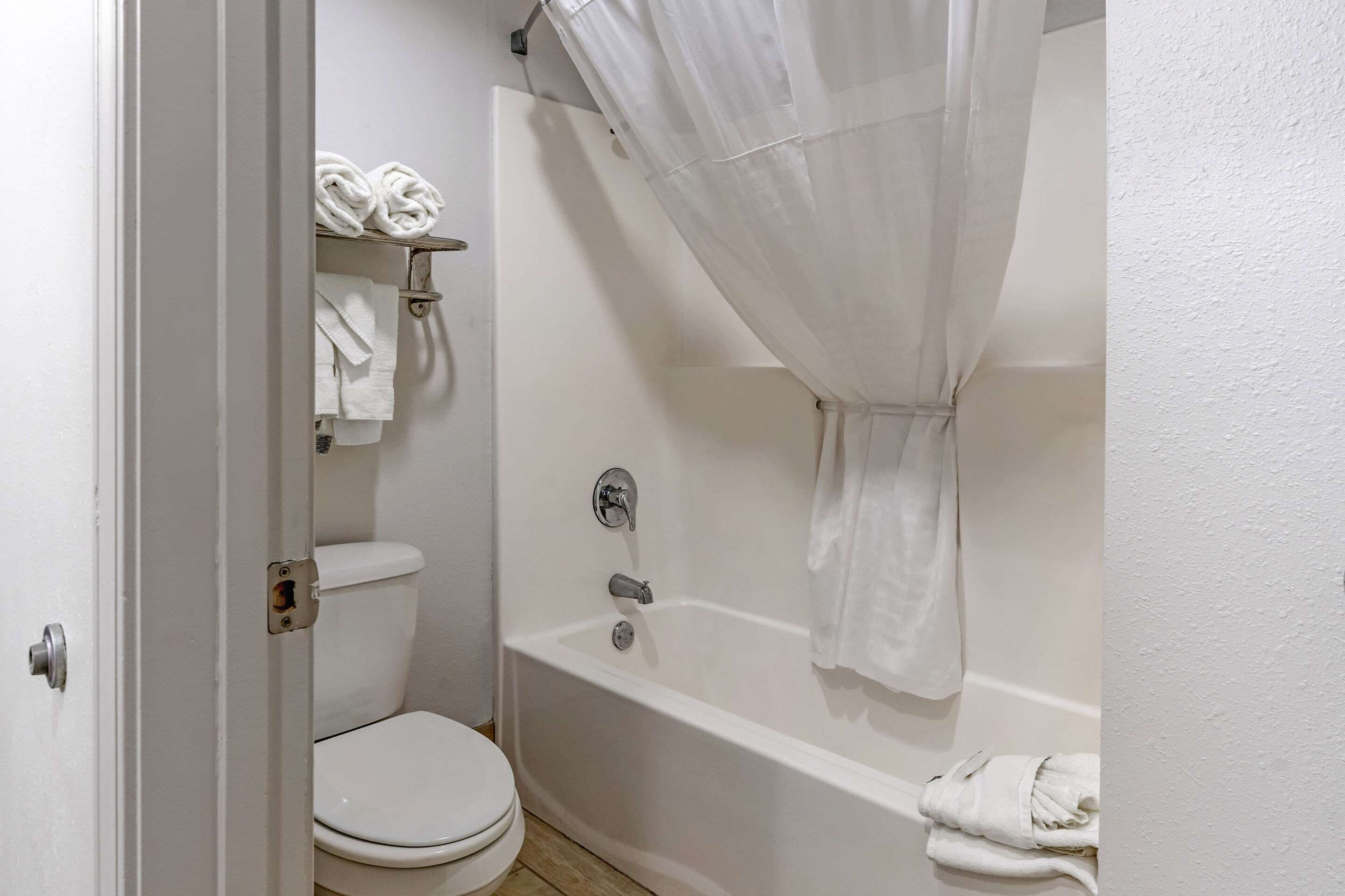 A bathroom with a white toilet, a bathtub with a shower curtain, and a towel rack with towels.