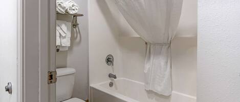 Un baño con inodoro blanco, bañera con cortina de ducha y toallero con toallas.