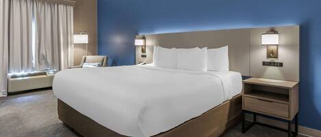 A hotel room with a large bed, two bedside tables with lamps, a chair, and a window with curtains.