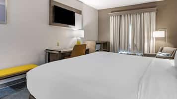 Una habitación de hotel con una cama grande, un escritorio con silla, un televisor montado en la pared y una ventana con cortinas.