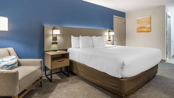 A hotel room with a large bed, a bedside table with a lamp, a chair, and a painting on the wall.