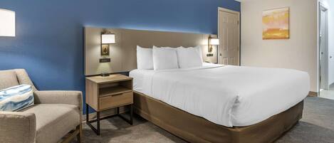 A hotel room with a large bed, a bedside table with a lamp, a chair, and a painting on the wall.