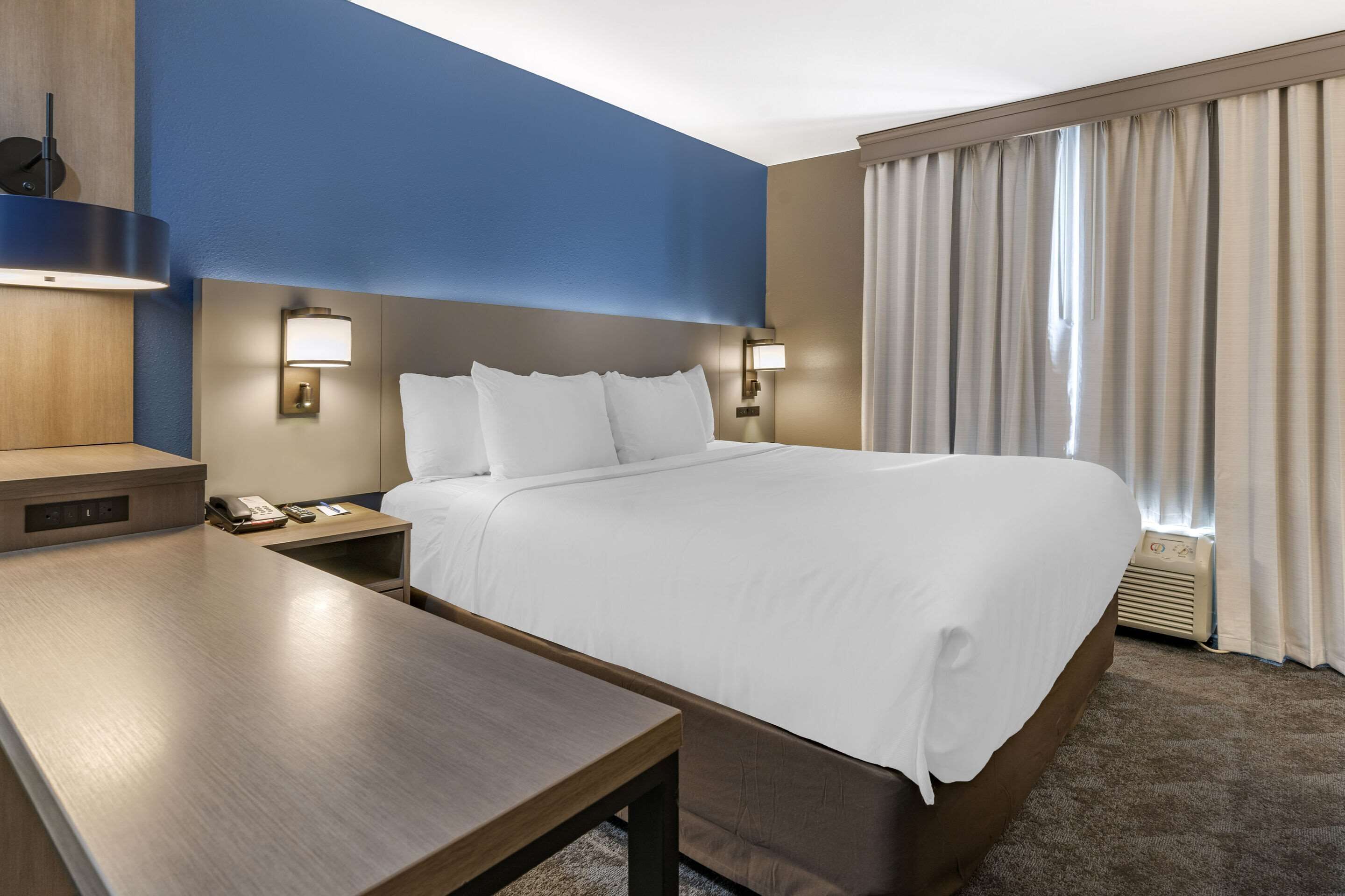 A hotel room with a large bed, bedside tables, a desk, and a window with curtains.