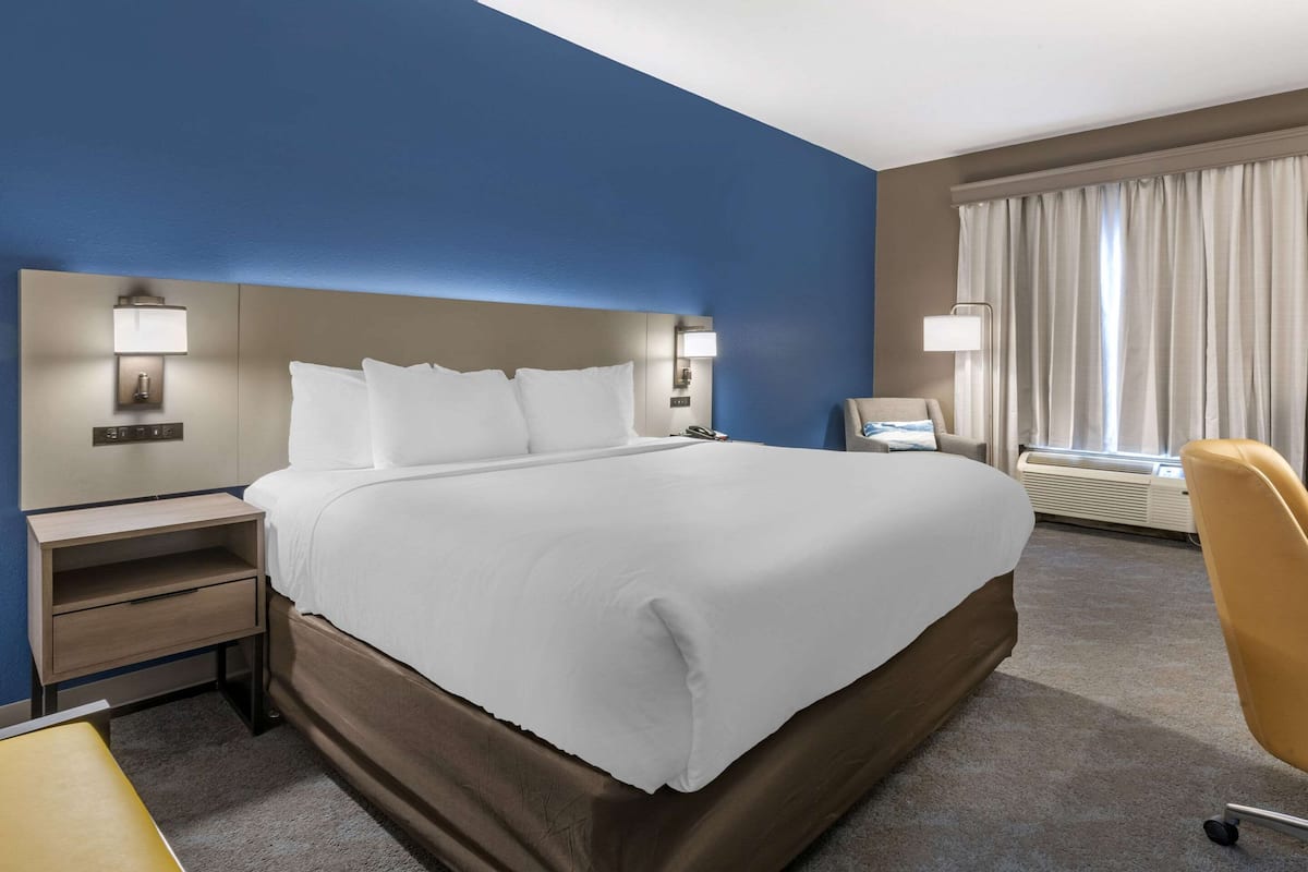 A hotel room with a large bed, bedside tables, a desk, a chair, and a window with curtains.