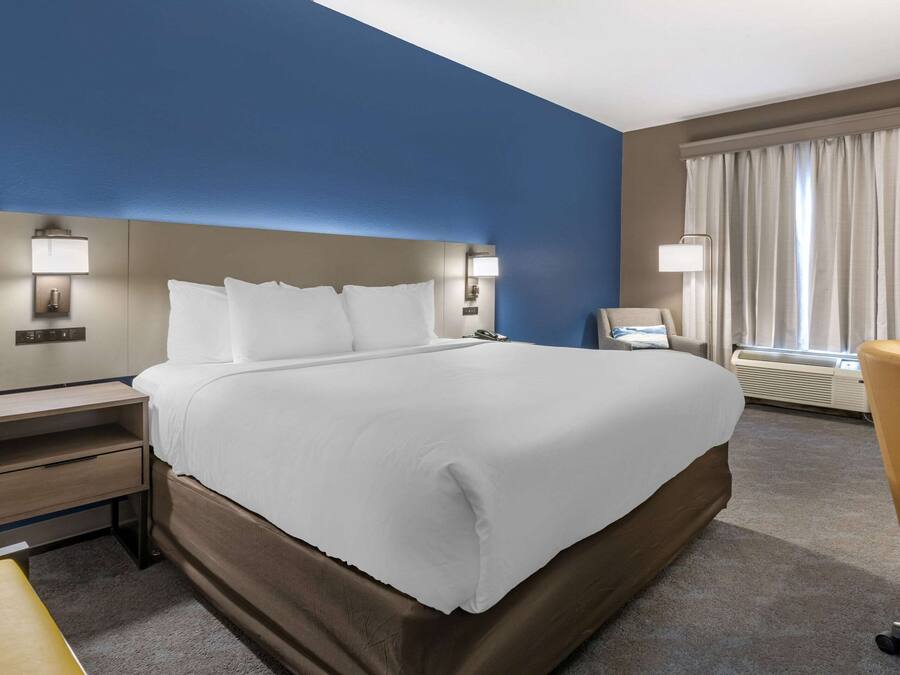 A hotel room with a large bed, bedside tables, a desk, a chair, and a window with curtains.