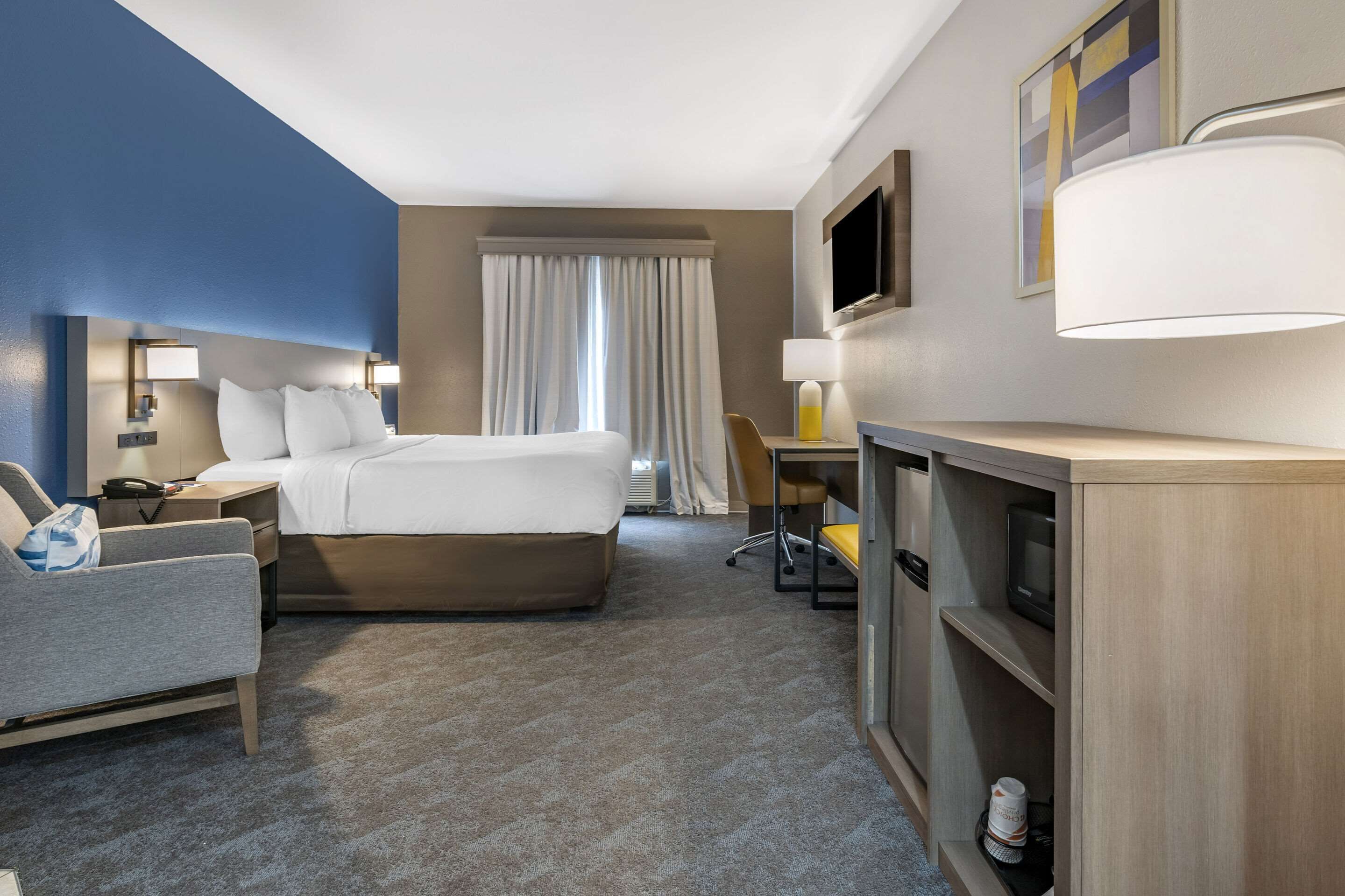 Ein Hotelzimmer mit Bett, Schreibtisch, Stuhl, Fernseher und Lampe.