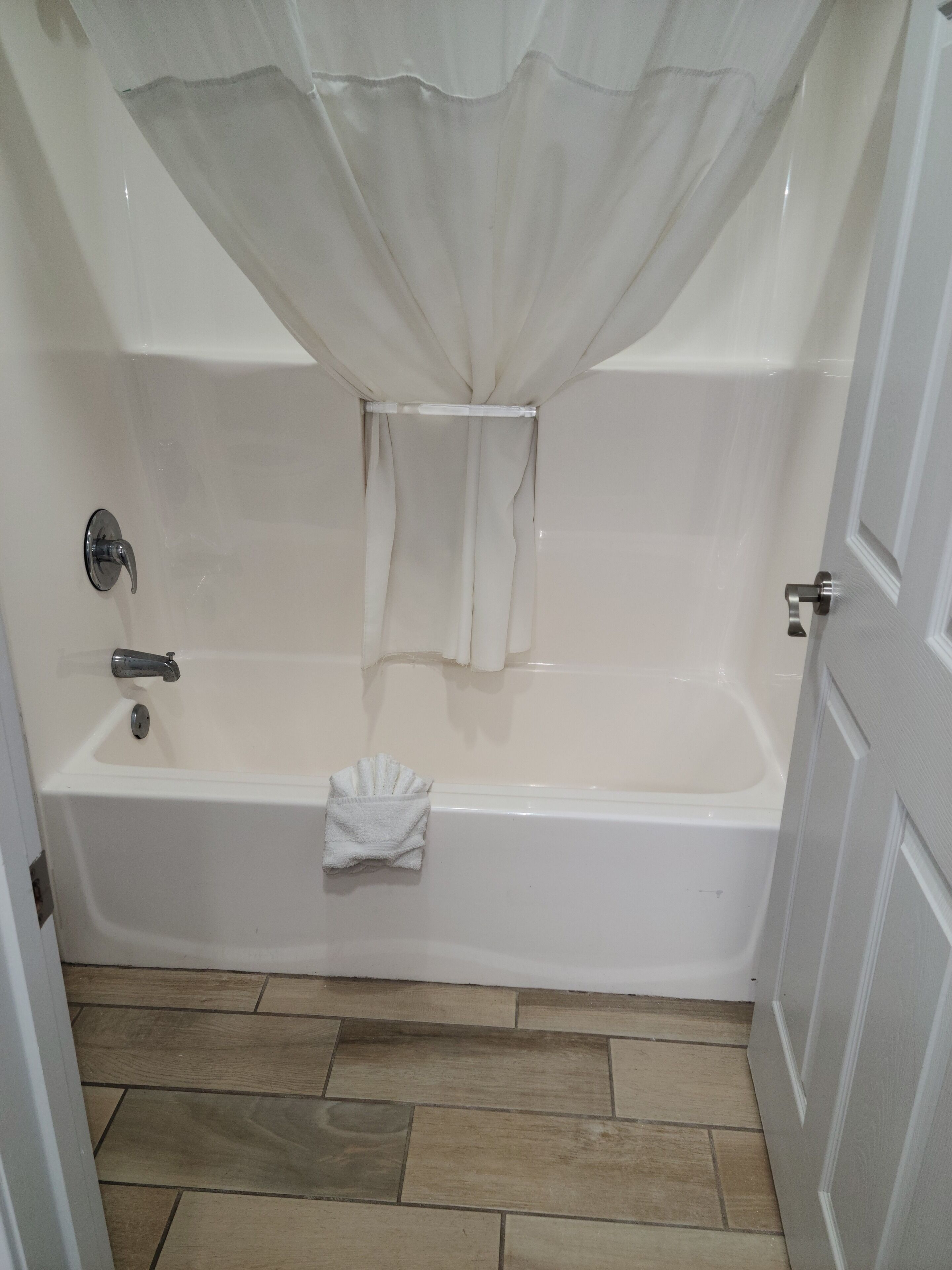 Un baño con bañera, cortina de ducha, toalla y puerta.