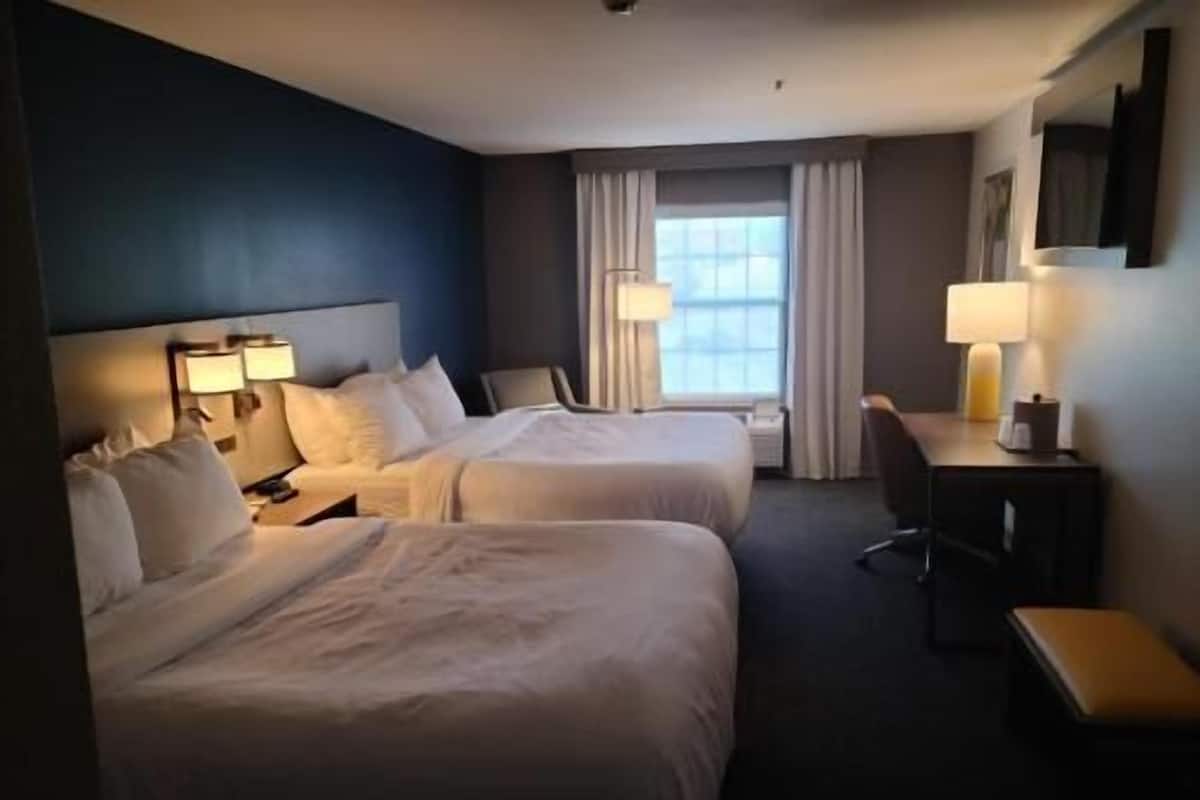 A hotel room with two beds, a desk, a chair, and a window with curtains.