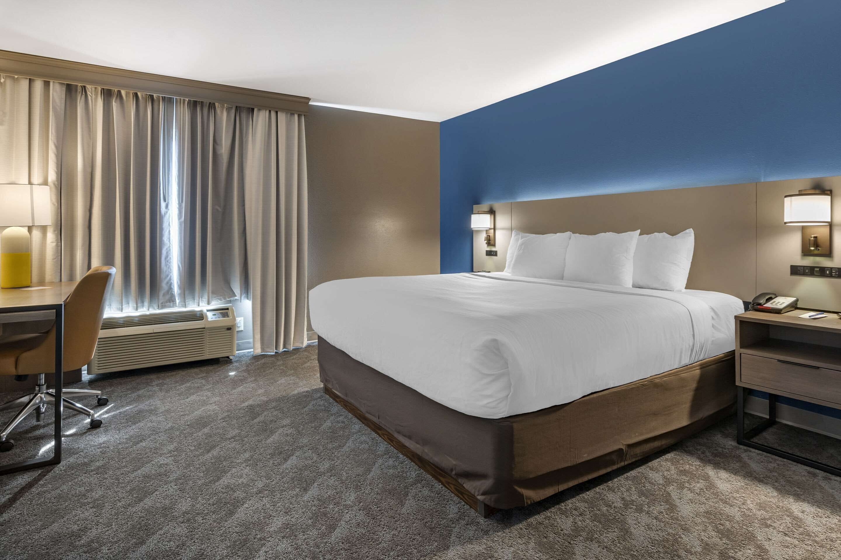 A hotel room with a large bed, a desk with a chair, a desk lamp, and a telephone.