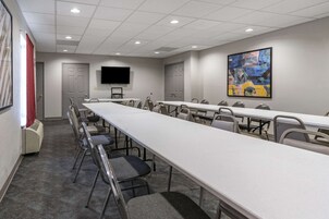 Uma sala de conferências com mesas compridas, cadeiras, uma TV de tela plana e um quadro na parede.