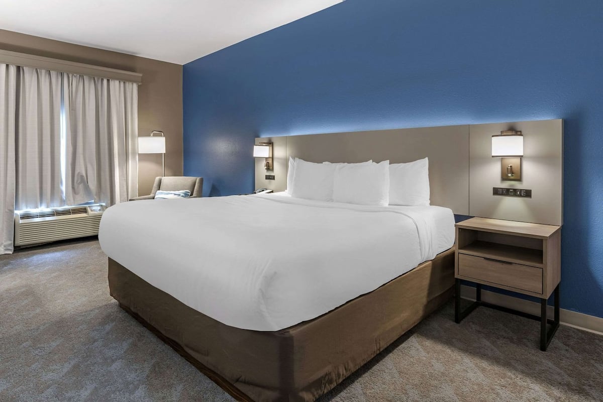 A hotel room with a large bed, bedside tables, a chair, a desk, and a window with curtains.