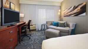 A hotel room with a flat-screen TV, a desk, a chair, a sofa, a bed, a lamp, and a painting on the wall. - Courtyard by Marriott Grand Junction (Grand Junction)