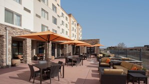 An outdoor patio with tables and chairs, orange umbrellas, and wicker furniture. - Courtyard by Marriott Grand Junction (Grand Junction)