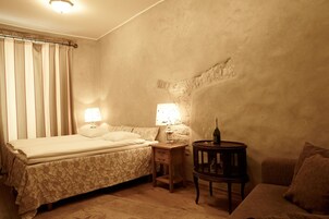 Een slaapkamer met een bed, twee bedlampen, een klein houten tafeltje met een fles en glazen, en een bank.
