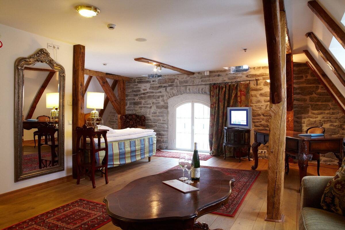 A cozy room with a bed, wooden beams, a stone wall, a television, and a dining area with a table and chairs.