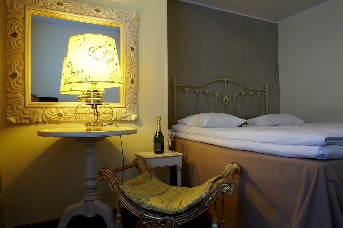 A hotel room with a bed, a bedside table with a bottle, a lamp, and a chair.