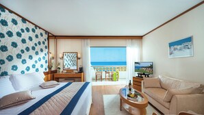 Ett hotellrum med en säng, en soffa, en TV, ett skrivbord och en balkong med utsikt över havet.