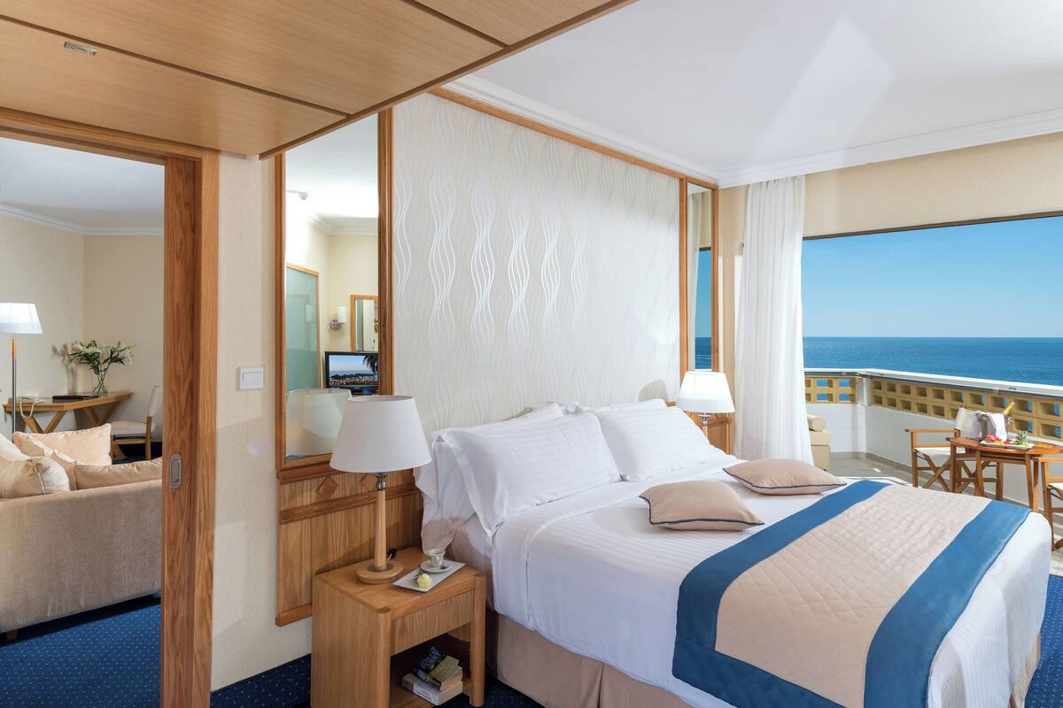 Une chambre d’hôtel avec un grand lit, des tables de chevet, un bureau et une vue sur l’océan.