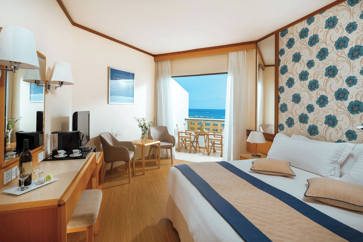 Une chambre d’hôtel avec un lit, un bureau, des chaises, une petite table et une vue sur l’océan.