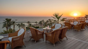 Eine Terrasse mit Korbmöbeln und Blick auf das Meer bei Sonnenuntergang.
